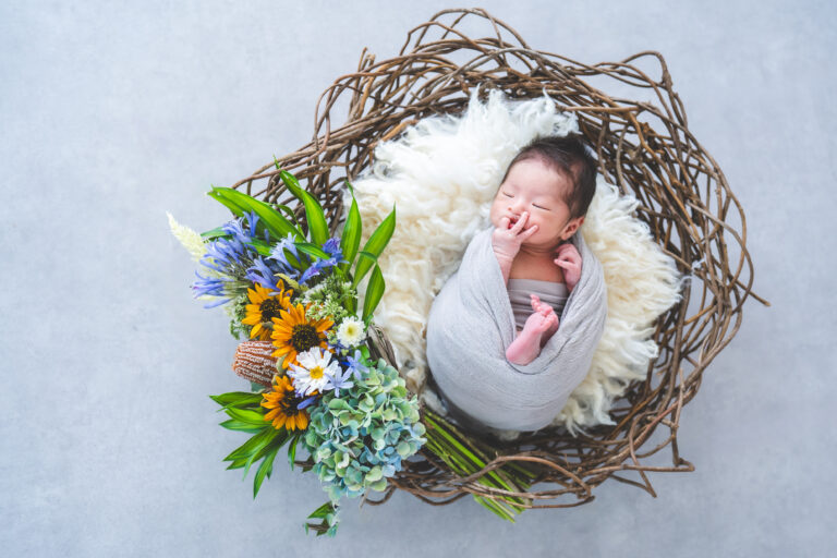 花に囲まれて眠る新生児の写真